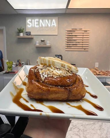 A caramel-glazed cinnamon roll topped with almonds and cream on a white plate