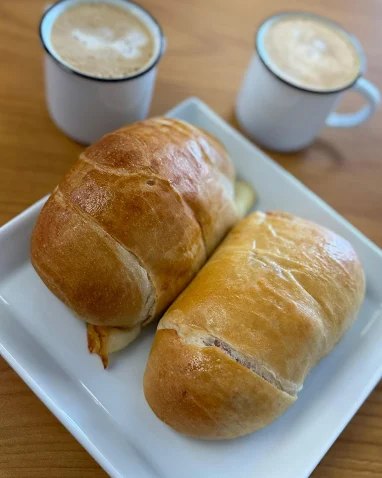 Two golden bread rolls on a plate with two cortados