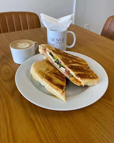 Pressed panini with ham and cheese beside a latte with leaf art